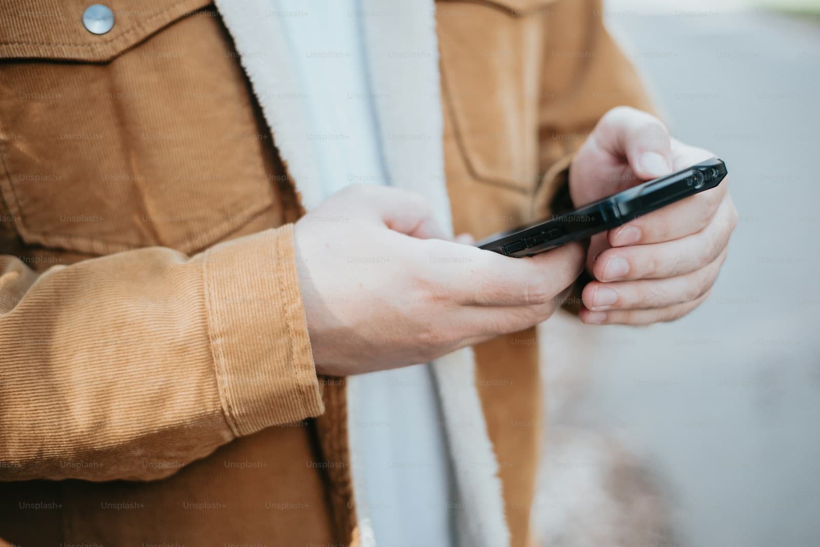 Person in a brown corduroy jacket looking down at a smartphone